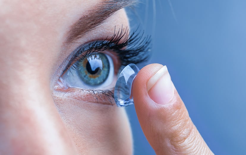 Close-up of an eye with a contact lens on a fingertip being brought towards it