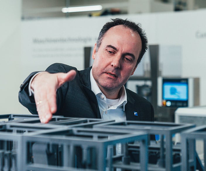 Mann in dunkler Jacke greift über ein Modell einer Verpackungsmaschine in einem Showroom