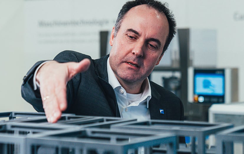 Man in a dark jacket reaching over a scale model of a packaging machine in a showroom