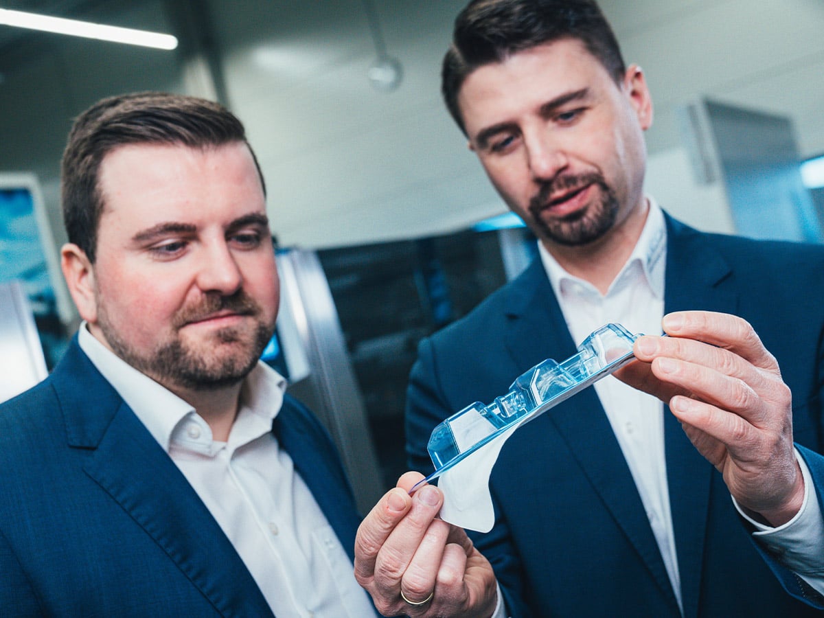 Two men in suits examining a transparent blue blister pack held between their hands