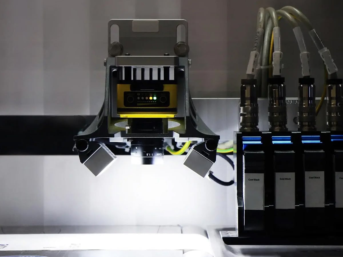 Vision system camera with side lighting over an inspection station, ink cartridges visible alongside