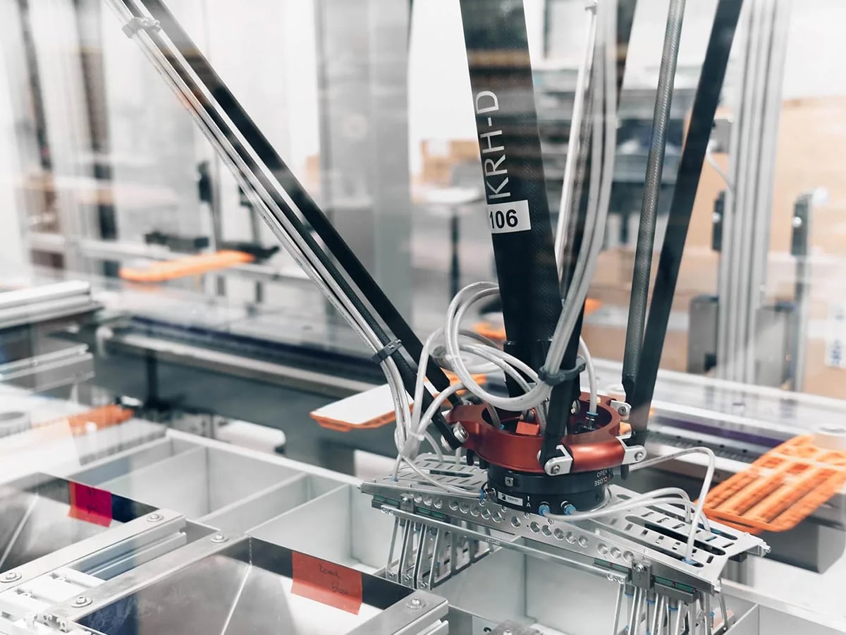 KOCH KRH-D delta robot with gripper over a sorting station, orange product carriers visible in the background