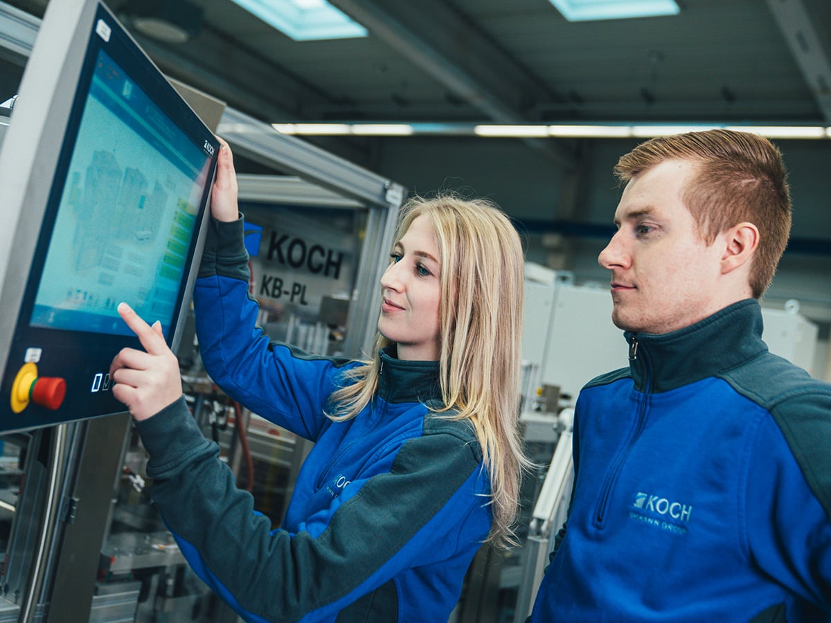 Two KOCH employees at a machine touchscreen displaying the KOCH Smart Analytics Dashboard