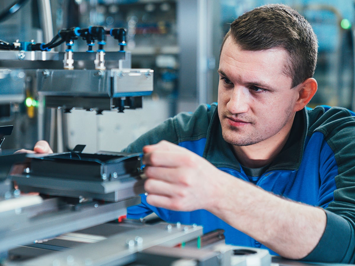 KOCH employee in blue work jacket adjusting a machine component with focused attention