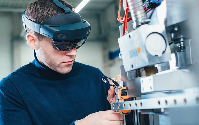 KOCH employee wearing a mixed reality headset connecting a sensor to a machine component