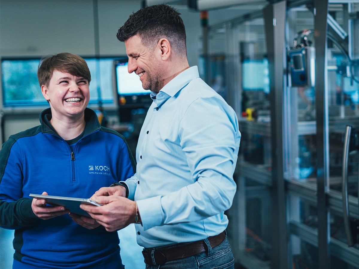 Two KOCH employees looking at a tablet together and laughing in a production hall
