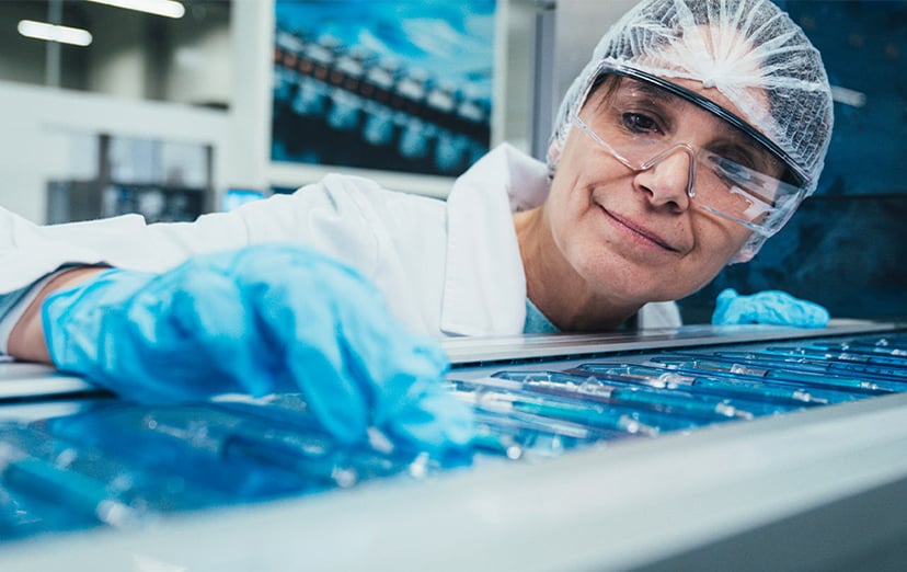 KOCH employee in cleanroom clothing closely inspecting a packaging machine station with blue-lit products