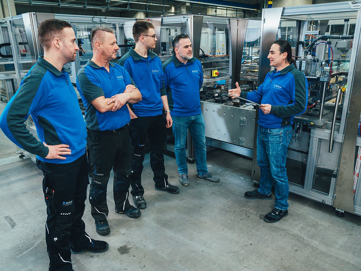 KOCH trainer addressing a group of four employees in front of a packaging machine during on-site training