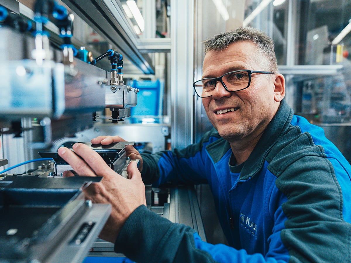 KOCH service technician working on a machine component, smiling at the camera