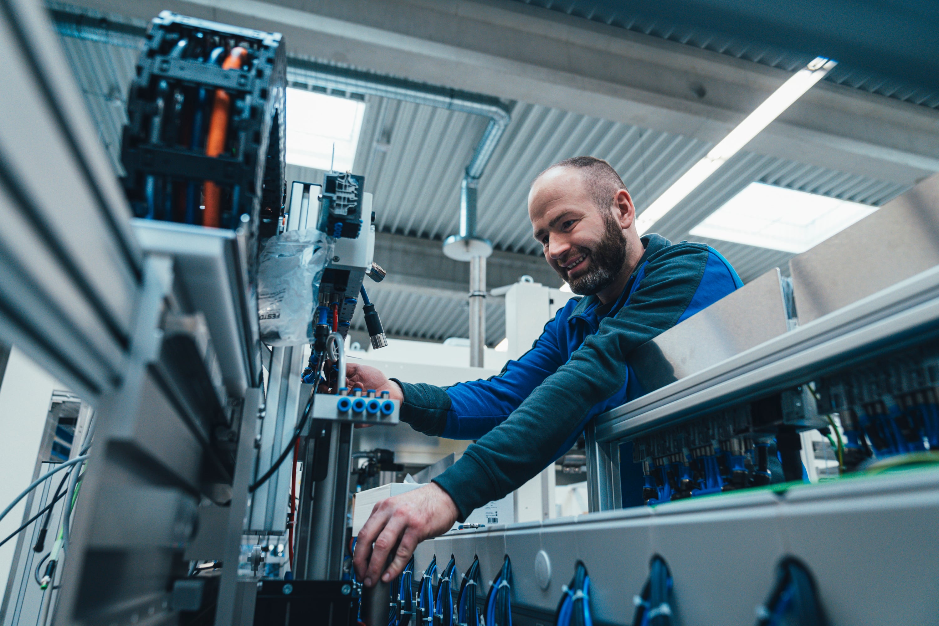 KOCH technician reaching into an open machine cabinet to adjust pneumatic components, smiling at the camera