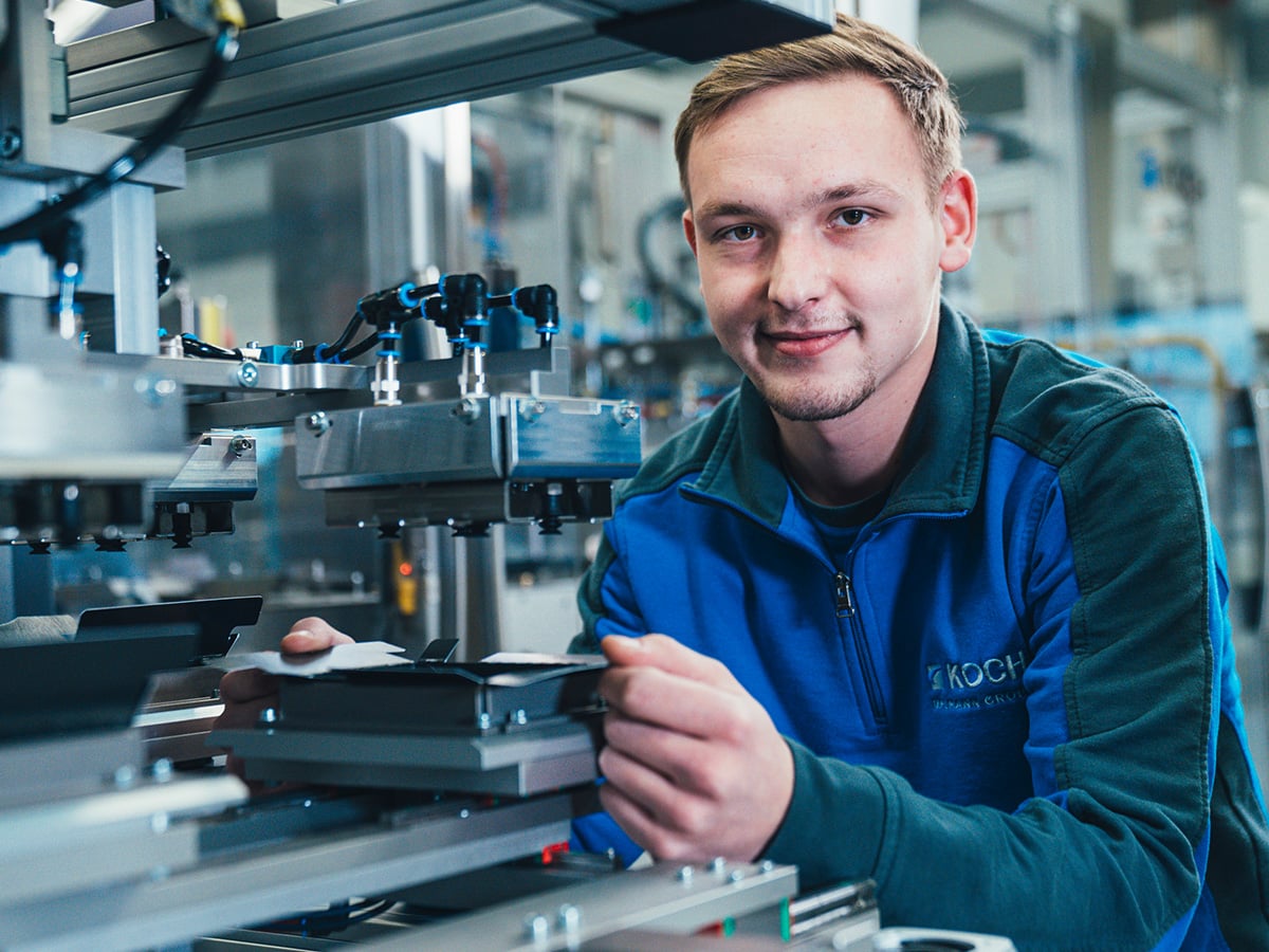 KOCH technician installing a format part on a packaging machine, smiling at the camera