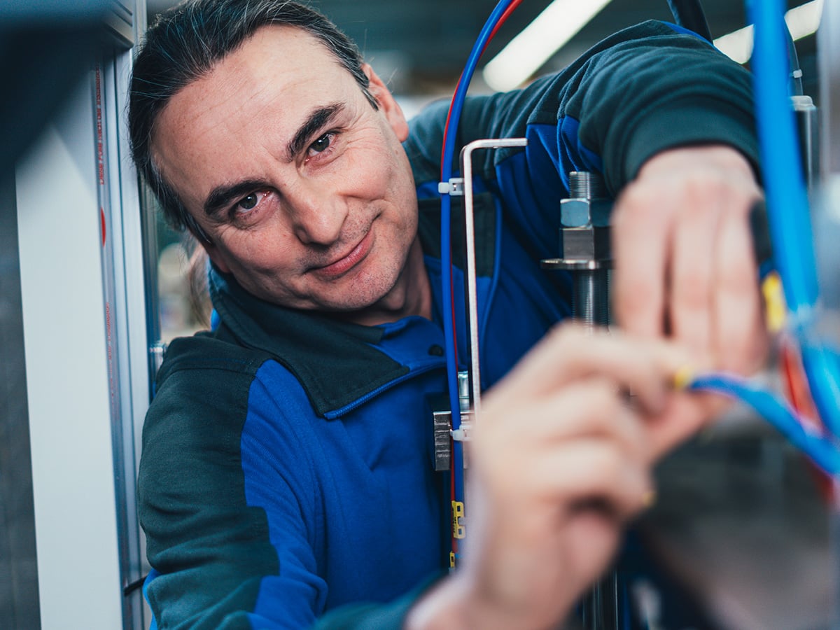 KOCH technician working on pneumatic cabling inside a machine cabinet, smiling at the camera