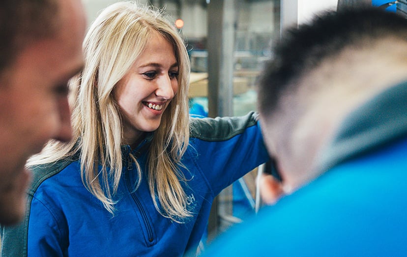 KOCH employee in blue work jacket smiling while working with two colleagues in a production environment