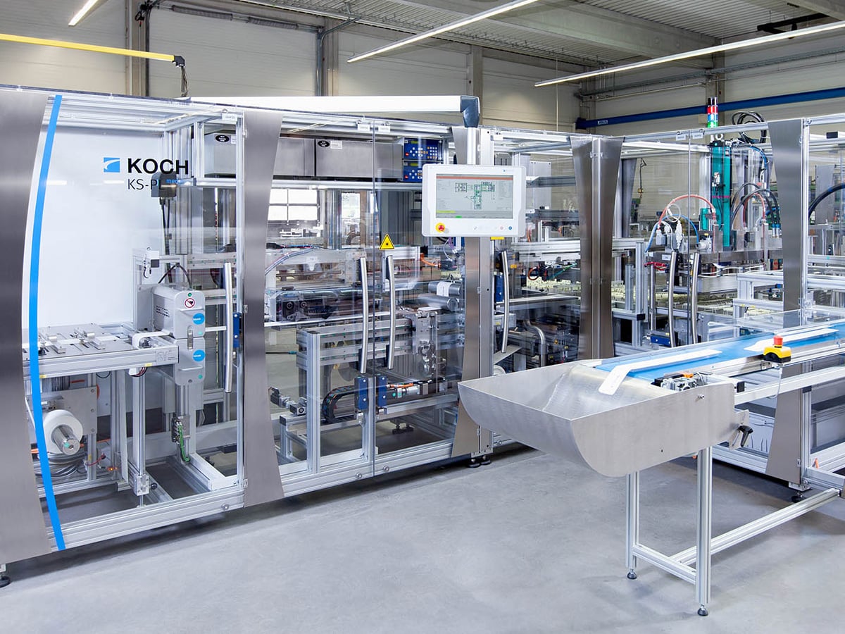 KOCH KS-P medplus sealing machine with glazed enclosure and discharge conveyor in a production hall