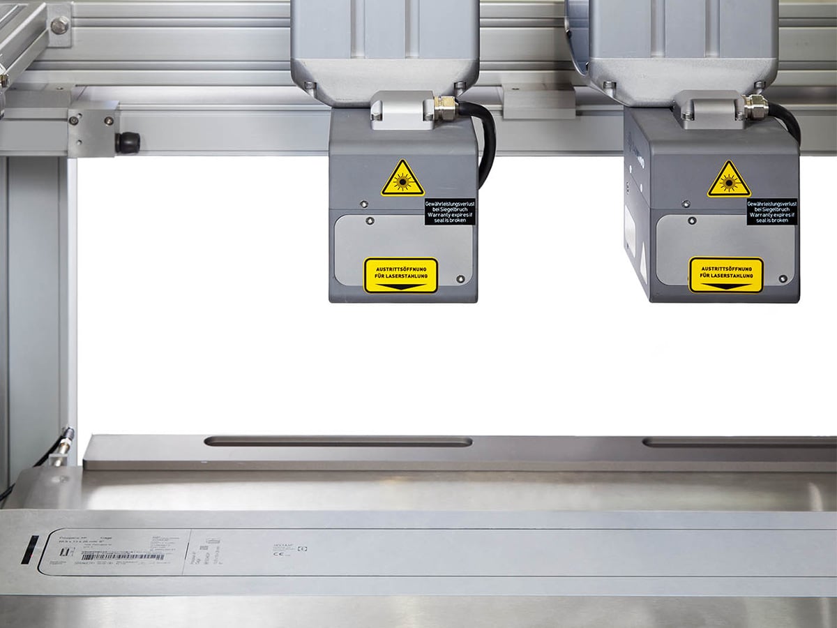 Two laser units mounted above a stainless steel tray for cutting Tyvek film to seal surgical packaging