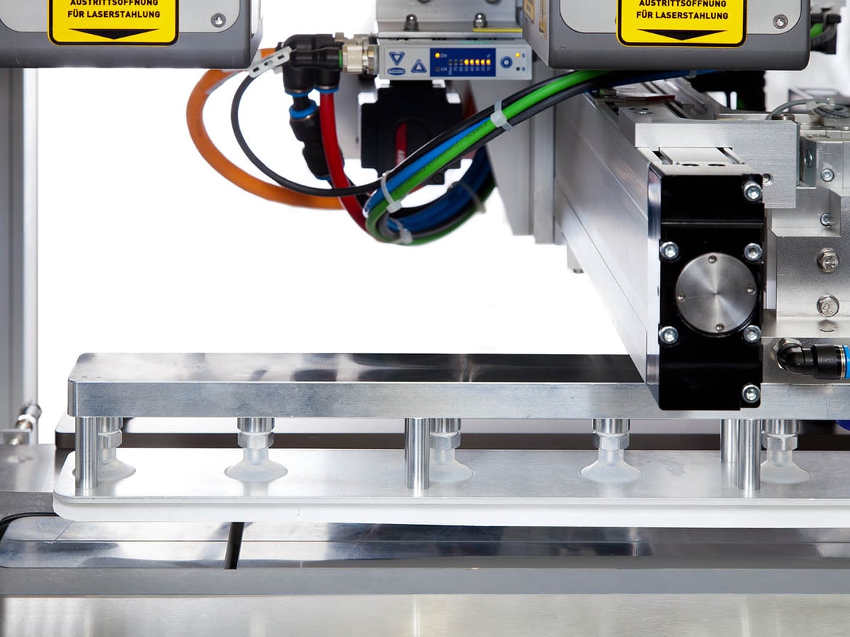 Transfer unit with suction cups picking up Tyvek film after laser cutting on a stainless steel surface