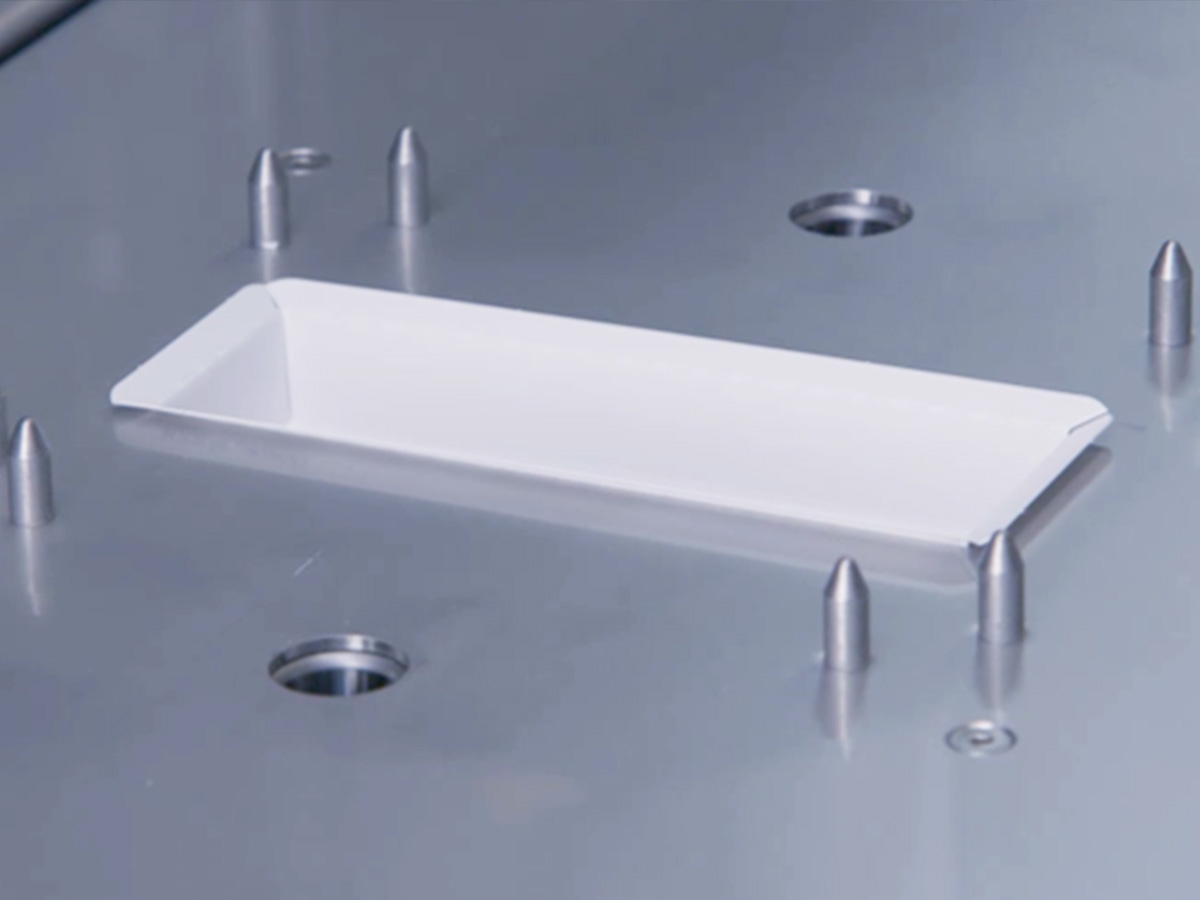 Single white rectangular tray held by guide pins on a stainless steel tooling plate