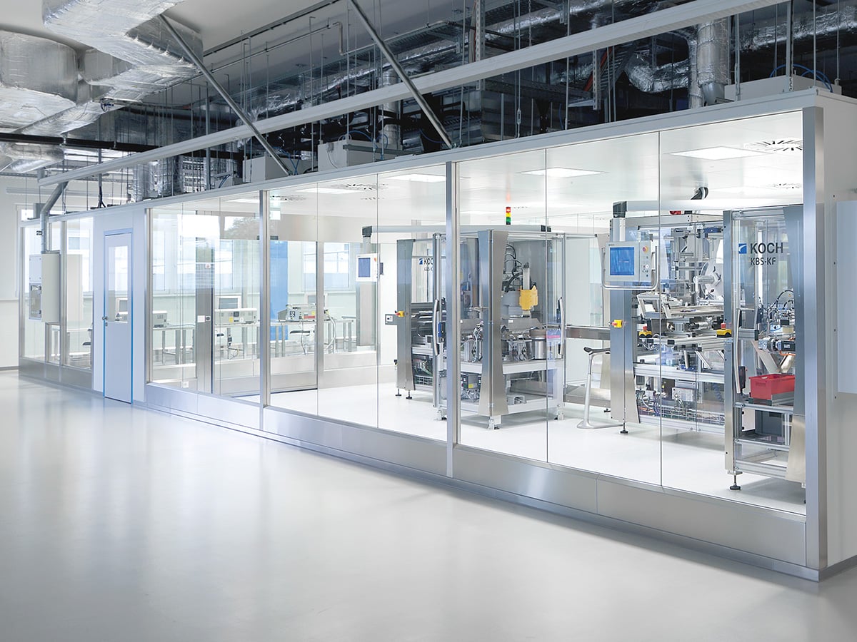 Glass-walled cleanroom seen from outside with a KOCH KBS-KF blister machine and further packaging modules