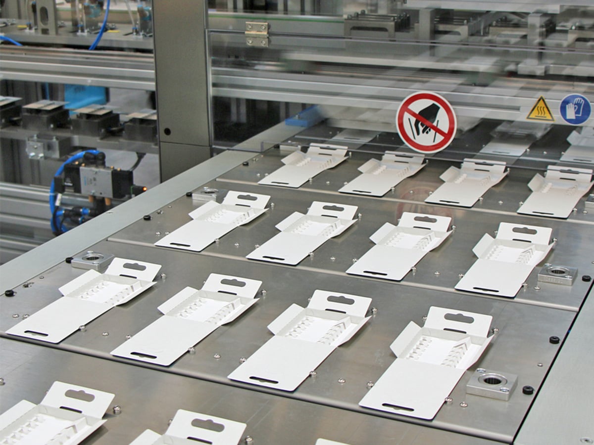 Rows of opened white cardboard packs on the stainless steel conveyor of a packaging machine