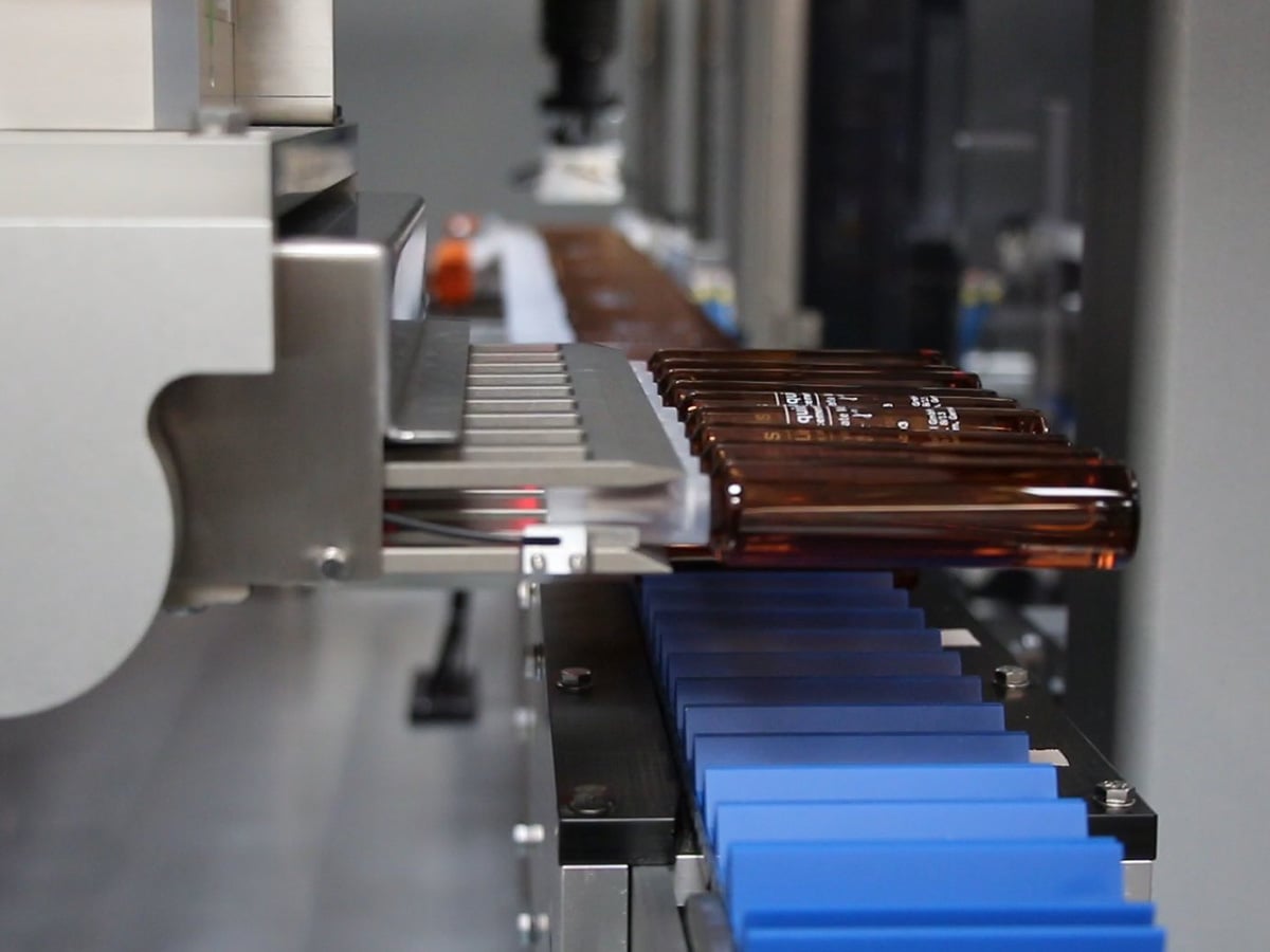 Brown glass ampoules lined up on a conveyor with separating fingers guiding them into position