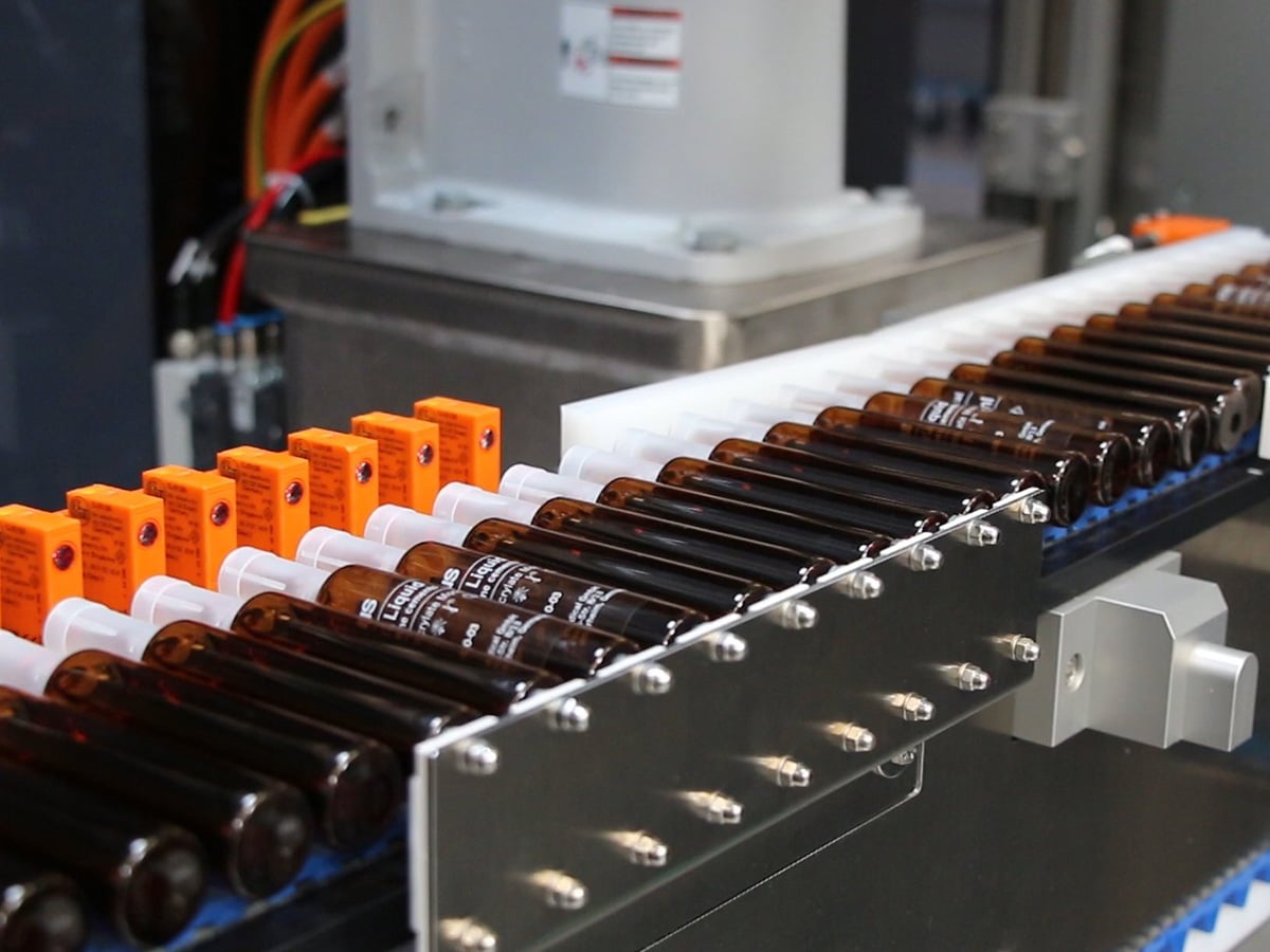 Brown glass ampoules aligned in white guide channels with orange sensors mounted alongside