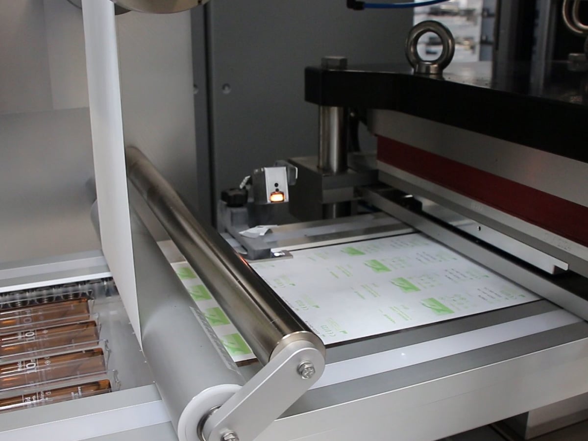 Printed lidding web running over a steel roller into the sealing station above the filled blisters