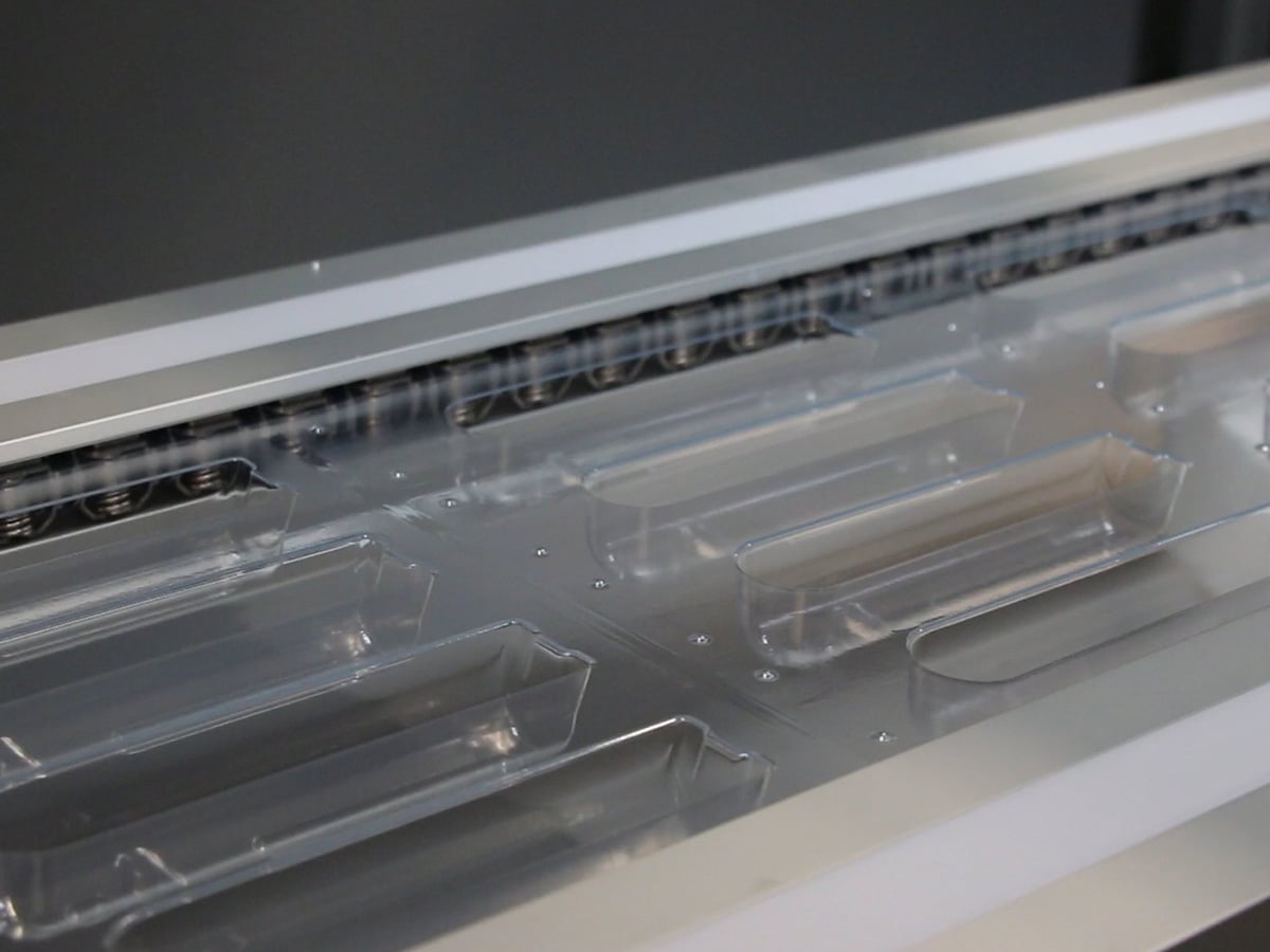 Transparent film web with rows of empty formed cavities running through a packaging machine