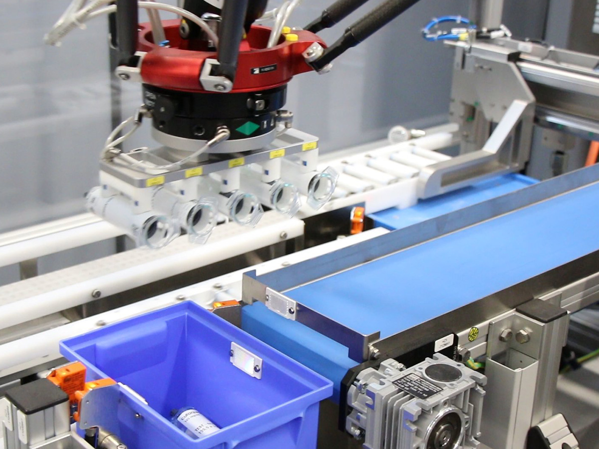 Robot arm lowering a six-station gripper over the conveyor belts of a packaging line