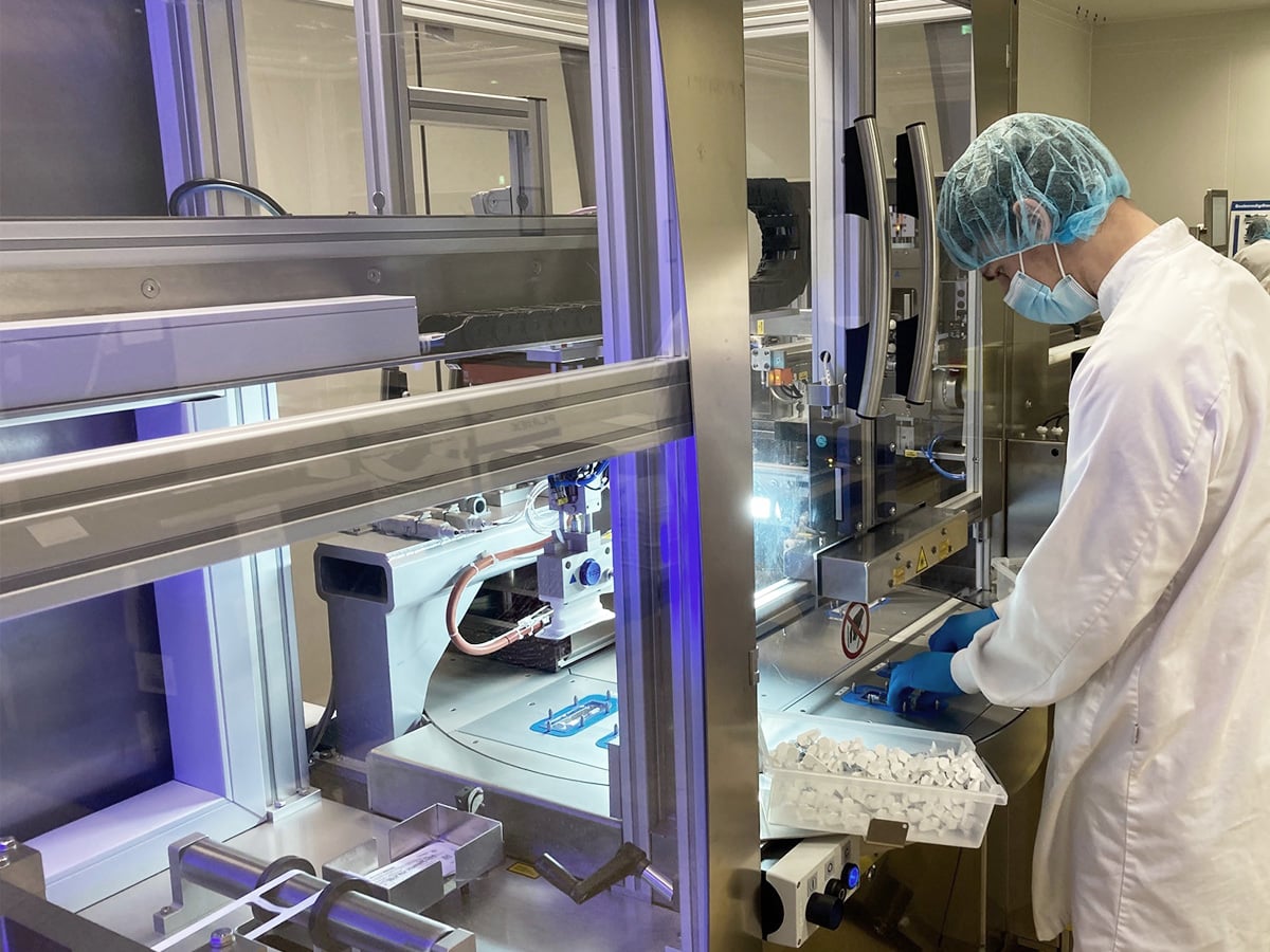 Person in cleanroom attire manually loading products from a container into the rotary table machine