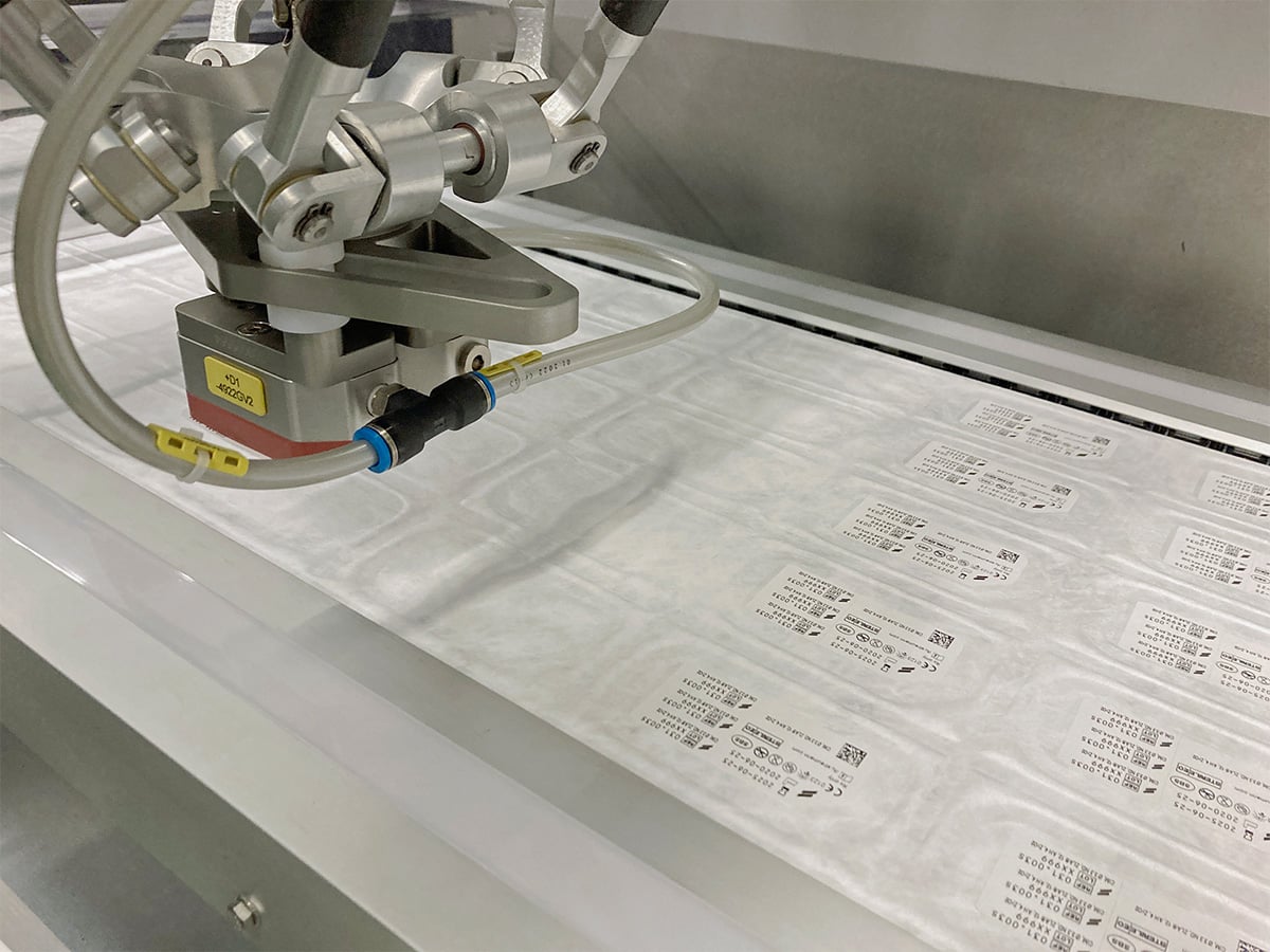 Delta robot arm above a row of sealed blisters with printed labels containing product data