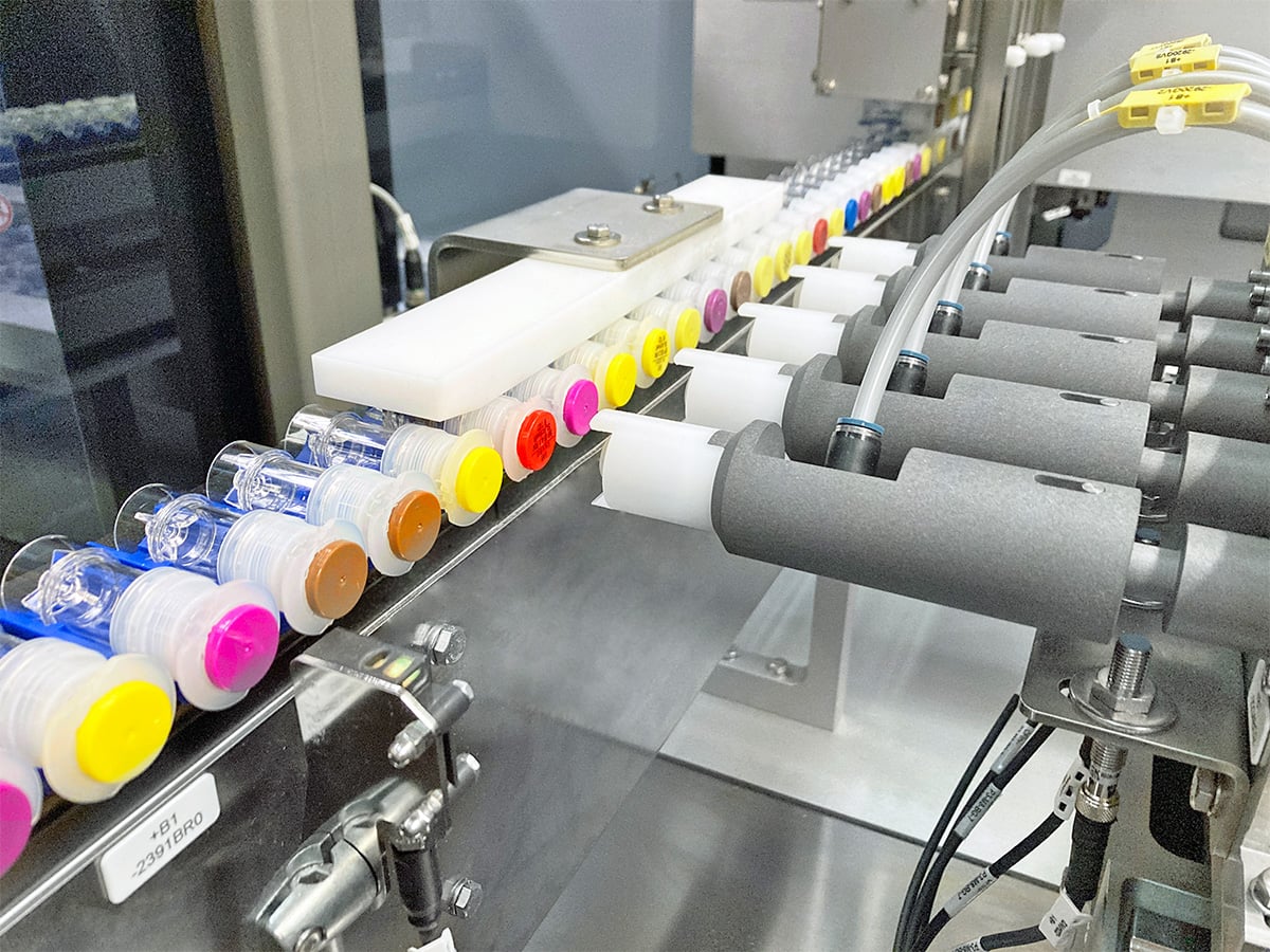Vials with coloured caps moving through an alignment station with rollers on a conveyor