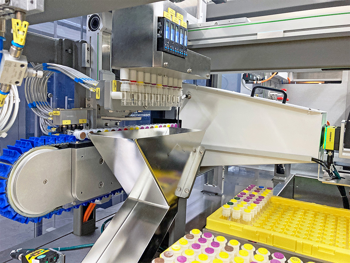Vials with coloured caps in yellow trays on a multi-component feeding and handling station