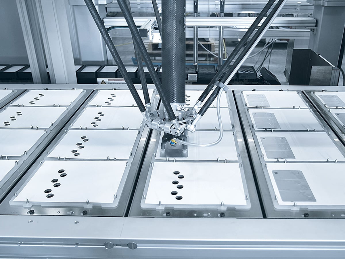Delta robot arm above a row of white blisters with round cavities on pallet transport pallets