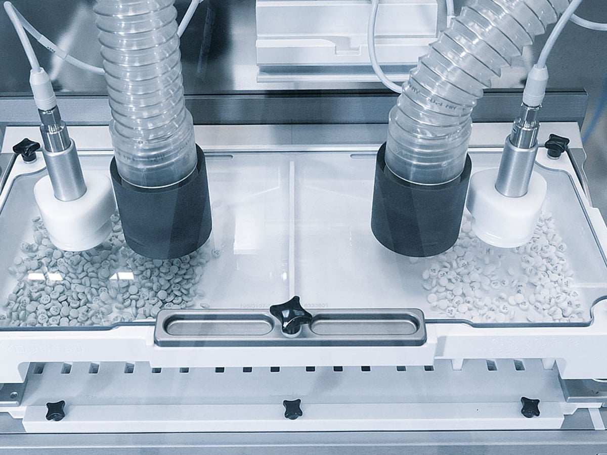 Two tablet feeding tubes above separate compartments of a blister filling station