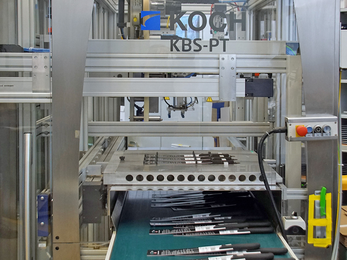 KBS-PT machine section showing knives in blister trays under a pressing bar with format pallets below