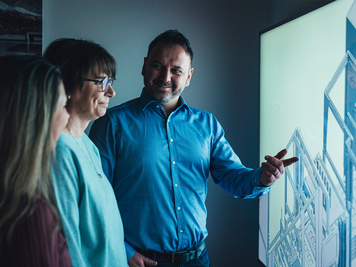 Two people discussing a packaging machine drawing on a wall