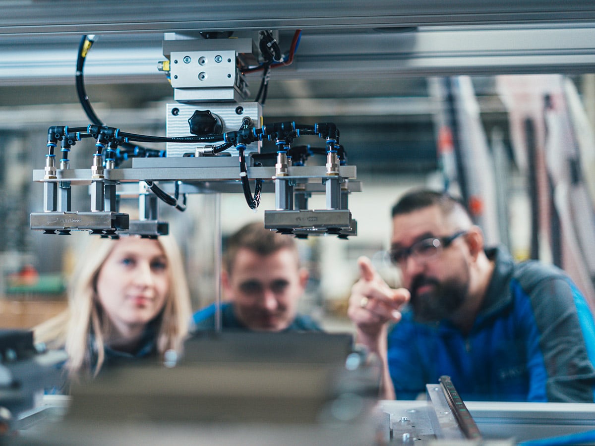 Three employees examining a pneumatic machine gripper together in a production facility at KOCH Pac-Systeme