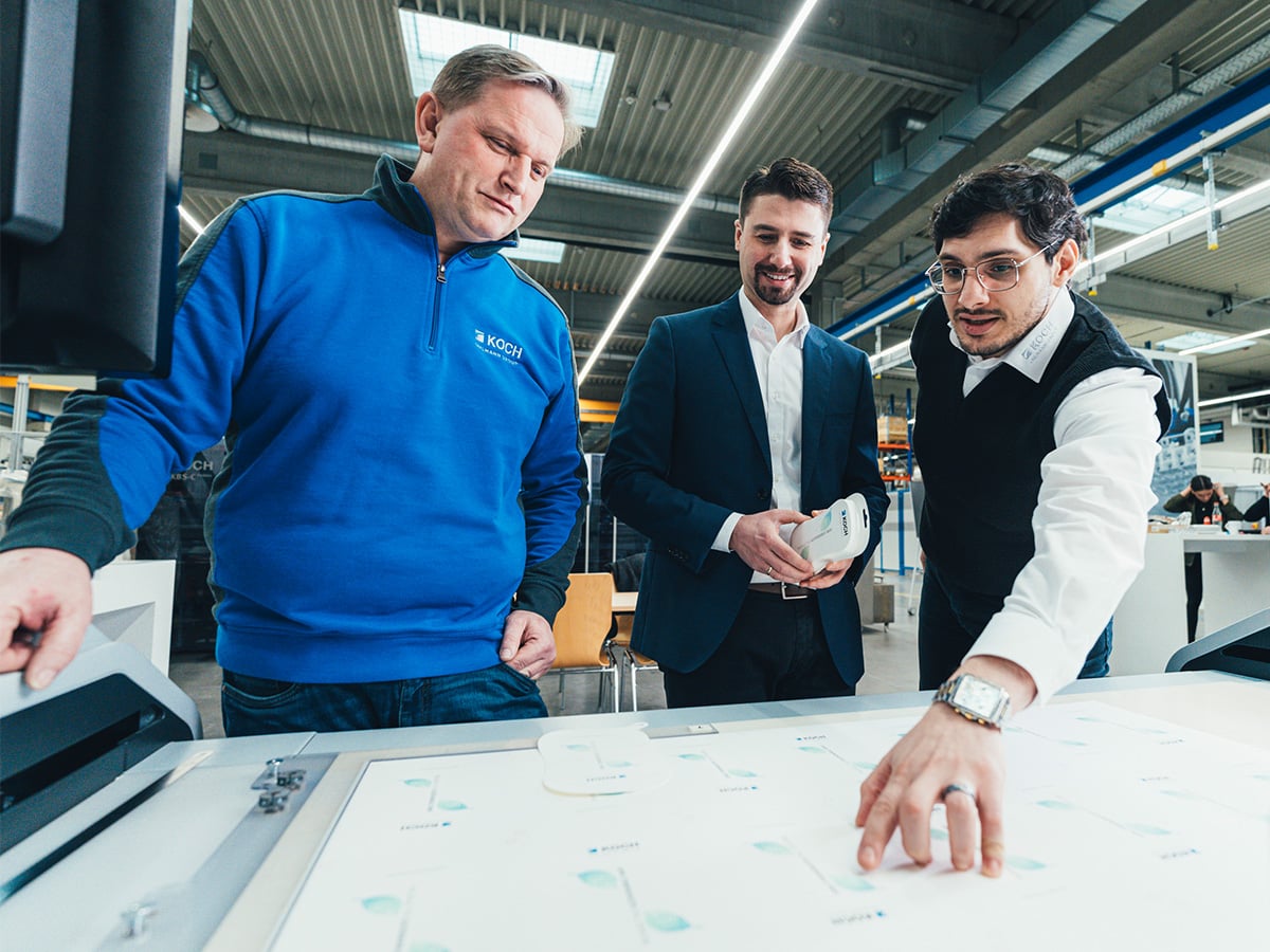 Three people reviewing packaging samples and process diagrams at the KOCH Packaging Competence Center, opened in 2023
