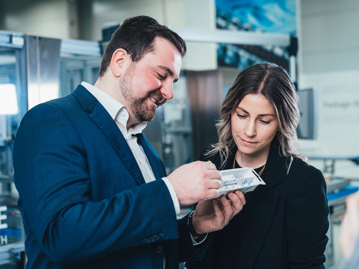 Two people examining a small packaging sample in a production environment, illustrating PPWR-aligned packaging development at KOCH Pac-Systeme in 2024