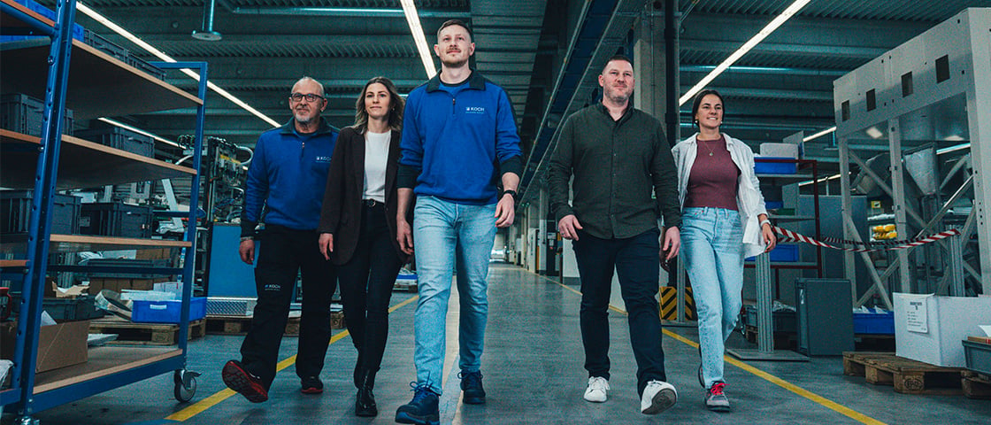Five KOCH Pac-Systeme employees walking together through a production hall, illustrating the company's vision and mission