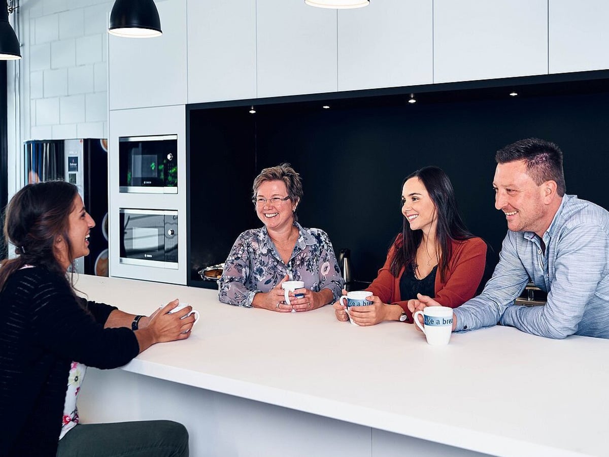 Four KOCH Pac-Systeme employees in conversation over coffee in a modern break room, illustrating the company's people-centred culture