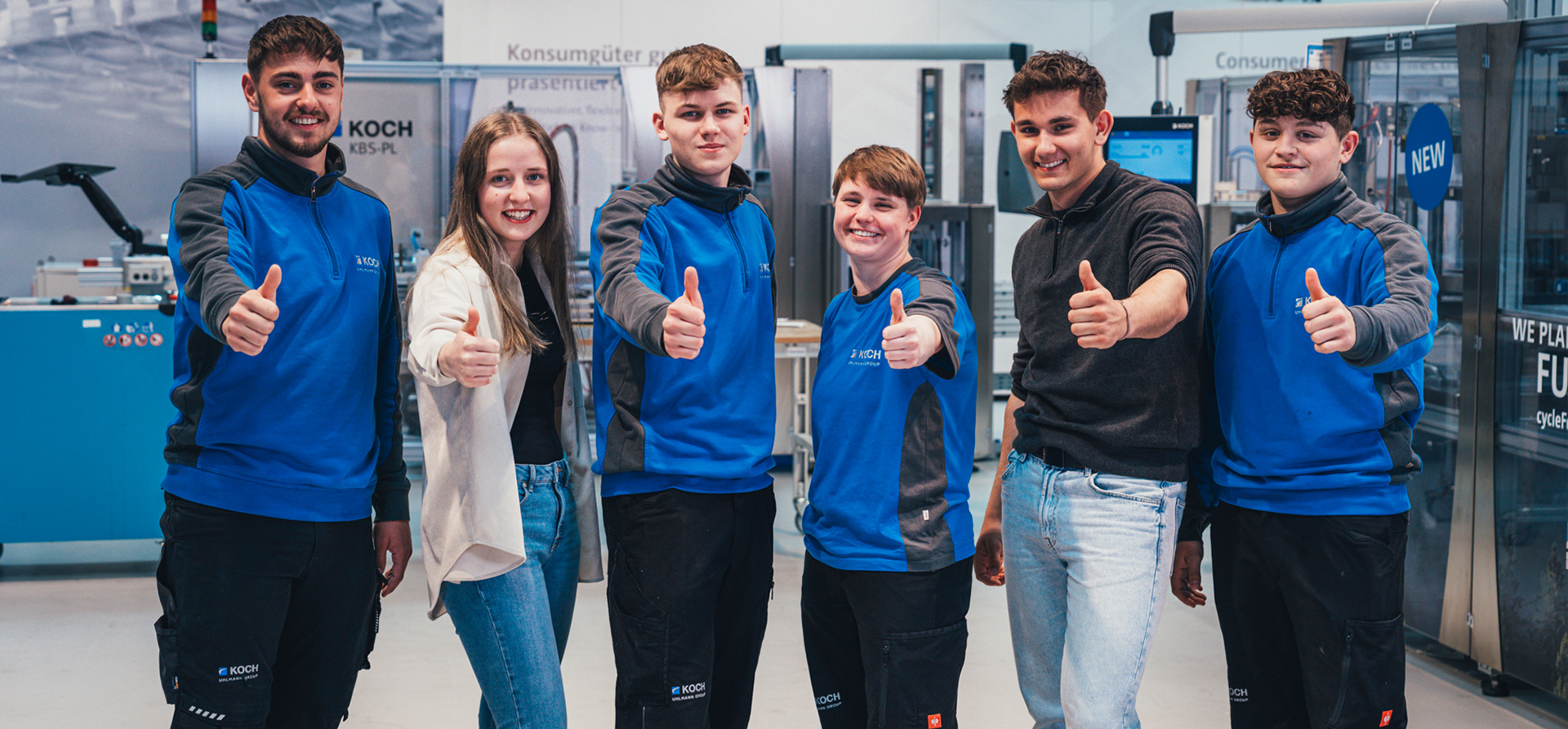 Group of KOCH Pac-Systeme apprentices giving thumbs up in a production environment, representing training opportunities at KOCH