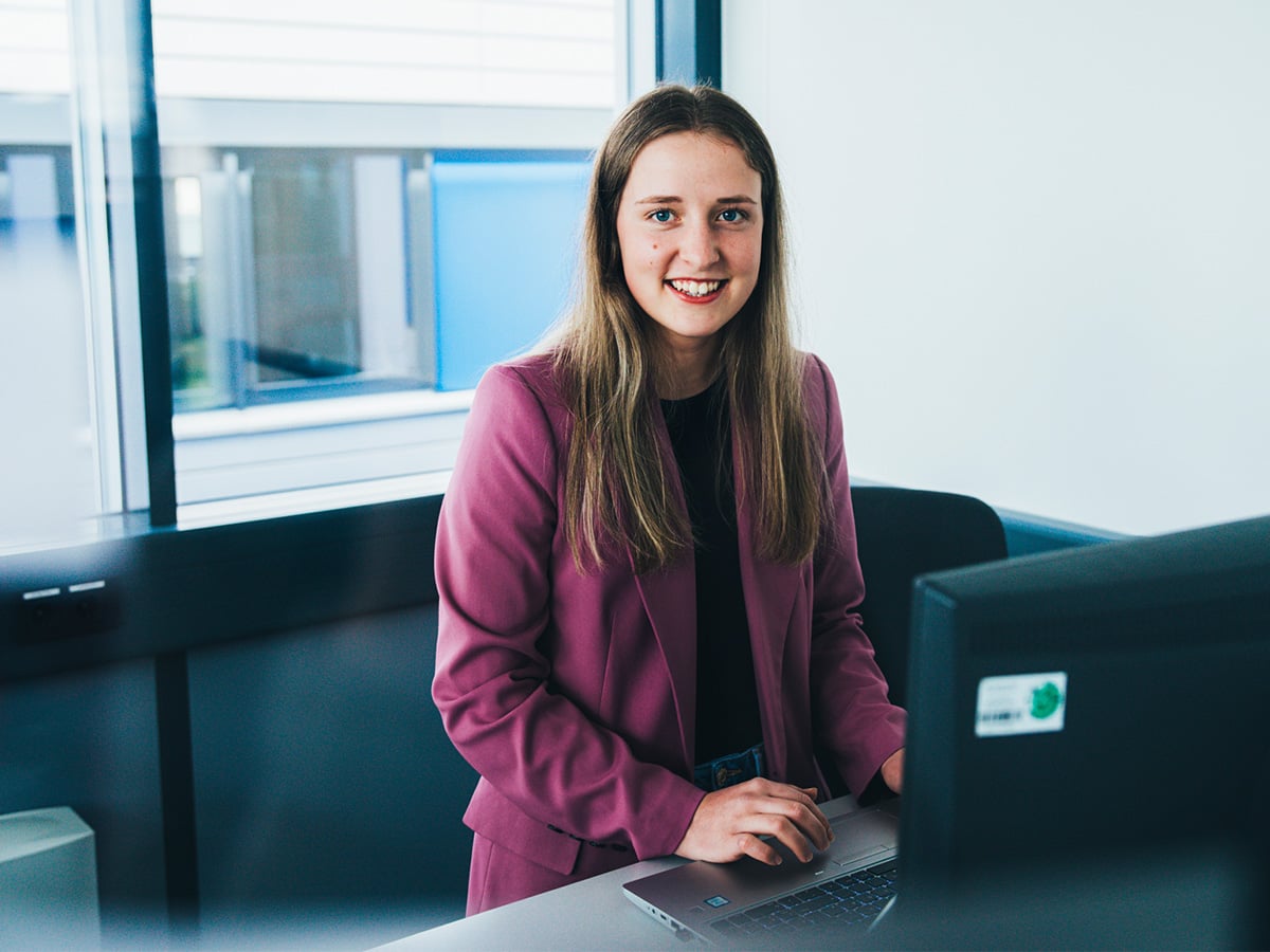 Young woman in a modern office environment with a laptop, representing the Industrial Clerk apprenticeship at KOCH Pac-Systeme