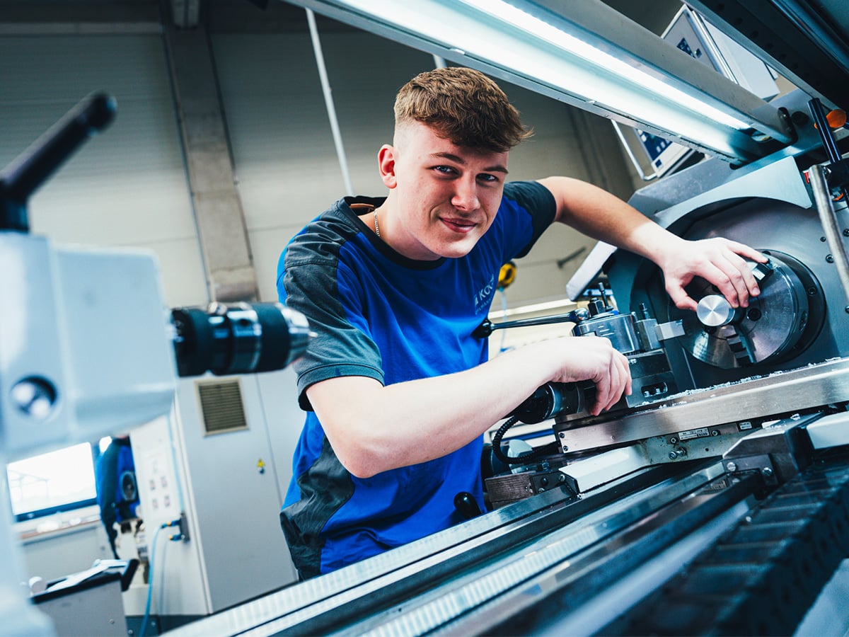 Young apprentice in blue KOCH workwear operating a machine tool in a production environment, representing the Industrial Mechanic apprenticeship