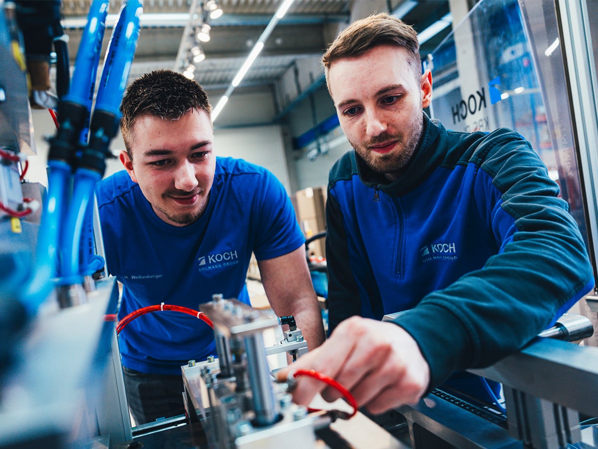 Two KOCH dual study students working together on electrical components of a packaging machine, representing the Bachelor of Engineering in Electrical and Information Engineering programme