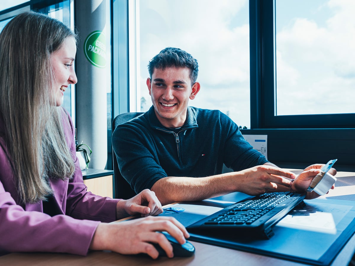 Two dual study students collaborating at a workstation in a modern office environment, representing the BWL-Industrial Business Management programme at KOCH Pac-Systeme