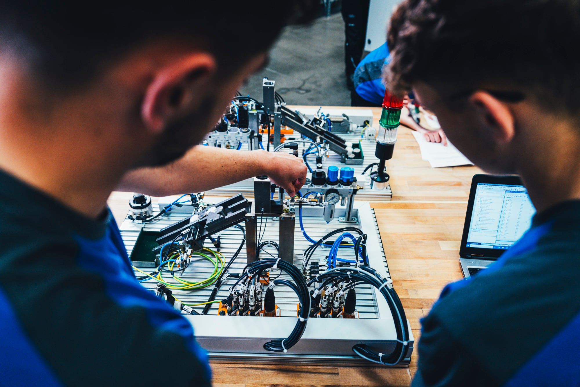 Two interns in blue KOCH workwear working on a technical assembly at a workbench, illustrating hands-on internship experience at KOCH Pac-Systeme