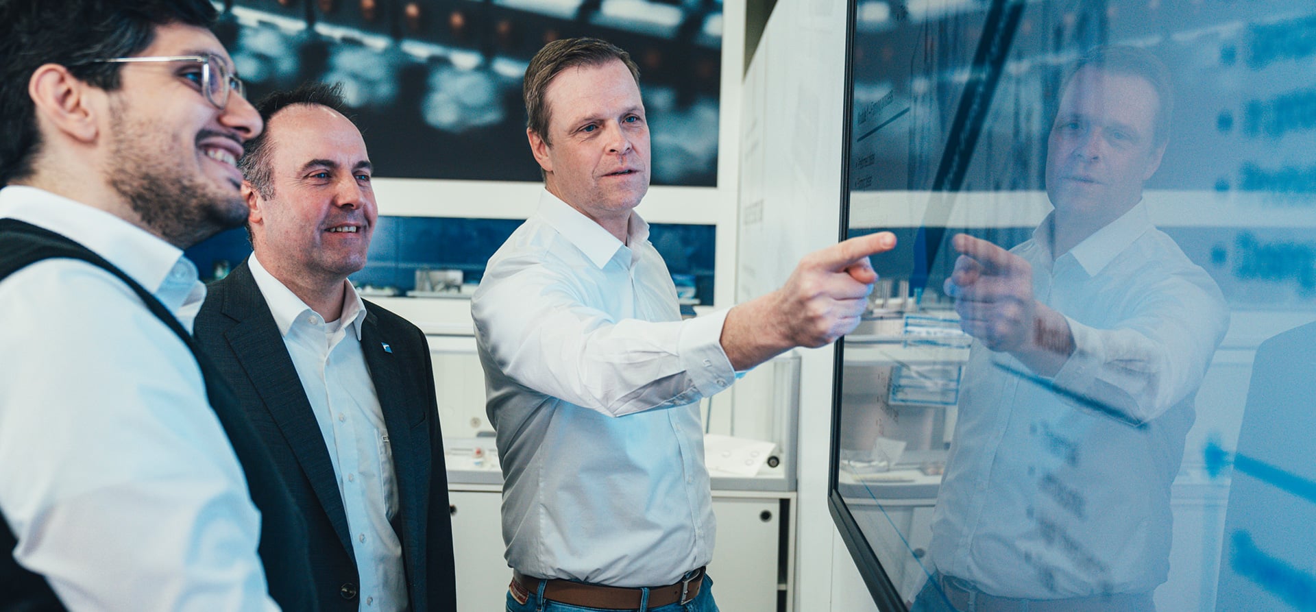 Three experienced KOCH Pac-Systeme professionals discussing technical content in front of a large screen in a modern environment
