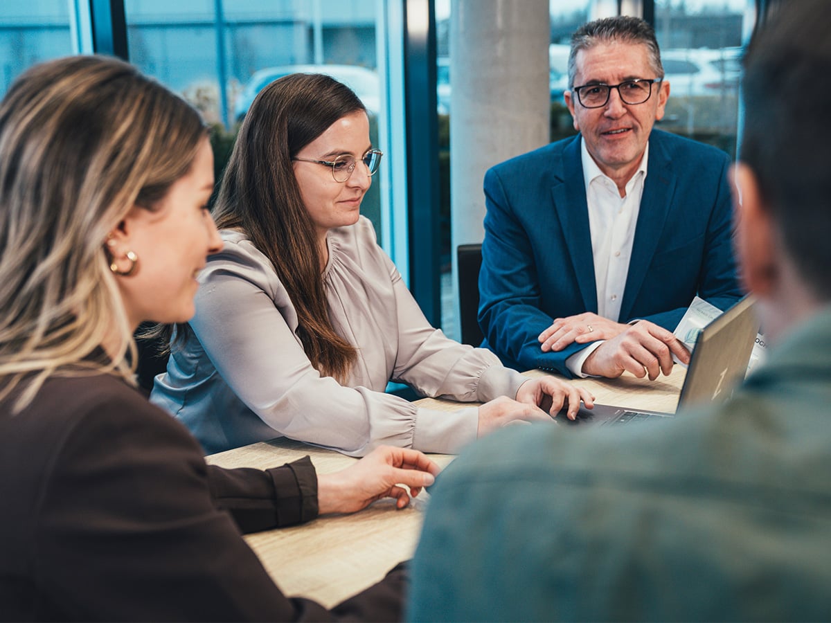 Three KOCH Pac-Systeme professionals in a meeting around a table, illustrating the collaborative working culture for specialists and managers