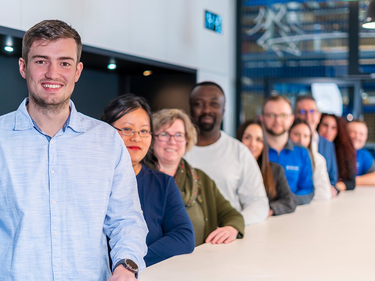 Diverse group of KOCH Pac-Systeme employees standing together at a table, representing the inclusive working culture and KOCHPlus benefits programme